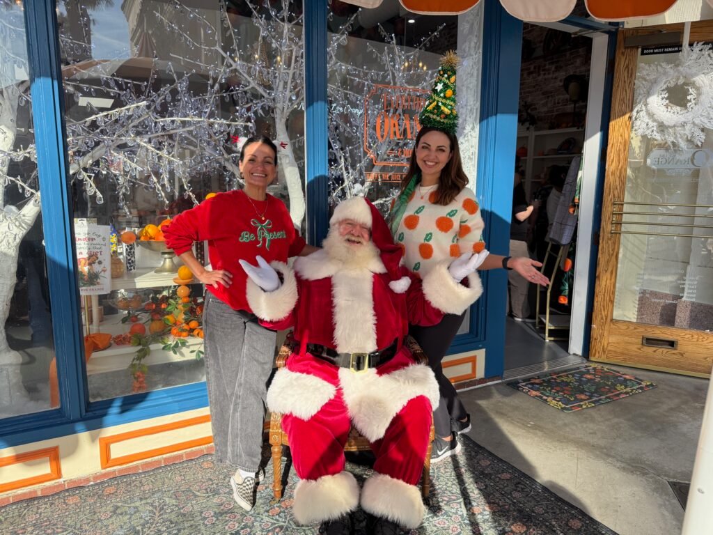Santa Claus poses with two women outside a decorated storefront