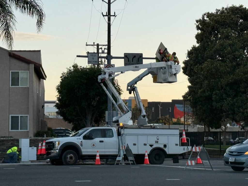 City crews in bucket lift repairing traffic signal near residential area in Orange.