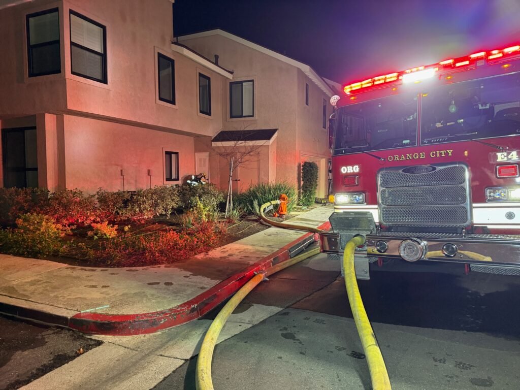 Orange City fire engine parked outside condo garage at night with hose lines stretched into the building.