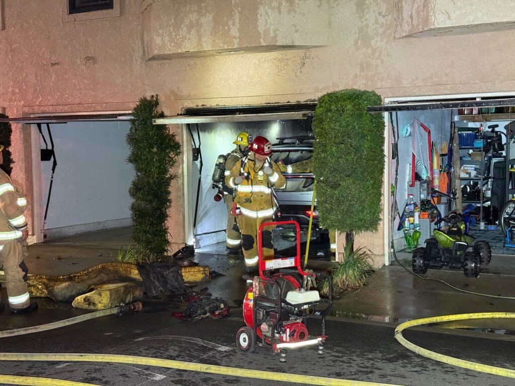 Firefighters working inside a garage beneath the condominiums with equipment and hose lines visible.