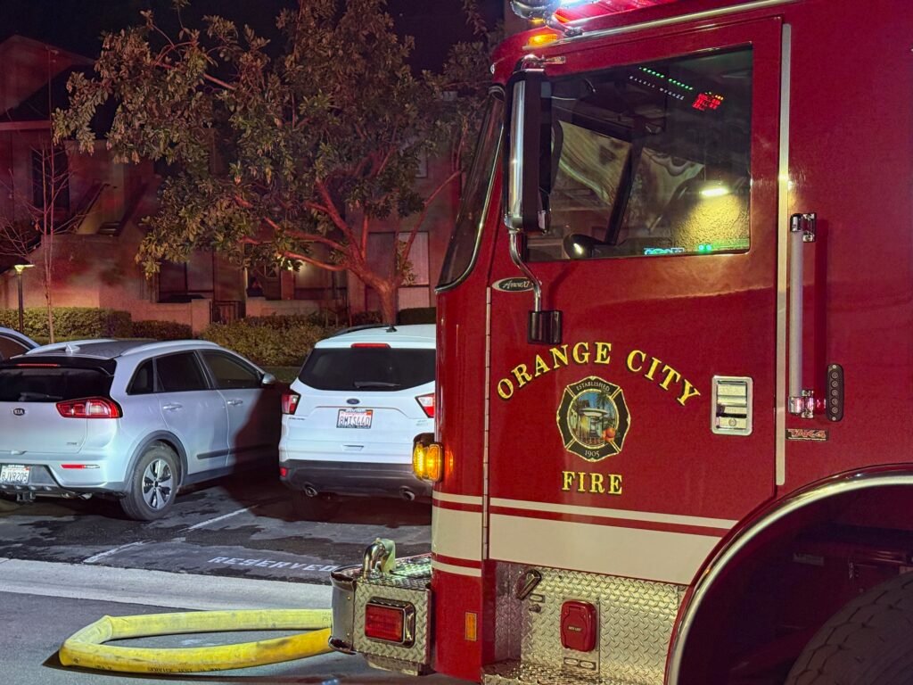 Close-up of Orange City Fire engine with hose lines on the ground near parked vehicles.