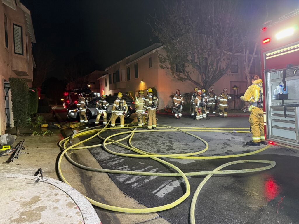 Multiple hose lines stretched across parking area as firefighters work at the Singingwood Street condo fire.