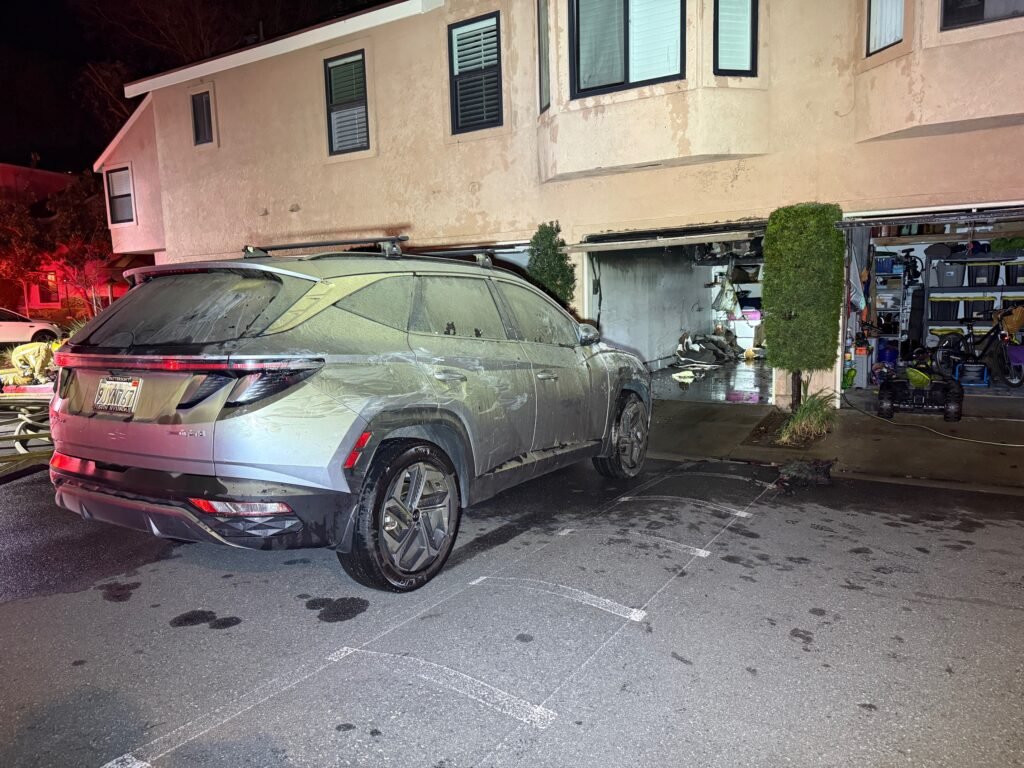 Vehicle covered in soot parked near damaged garage following fire at 155 N Singingwood Street.