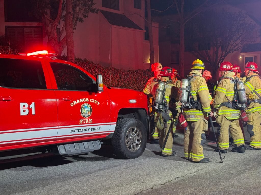 Orange City Fire Battalion Chief vehicle with firefighters gathered nearby at the Villeurbanne condo fire scene.
