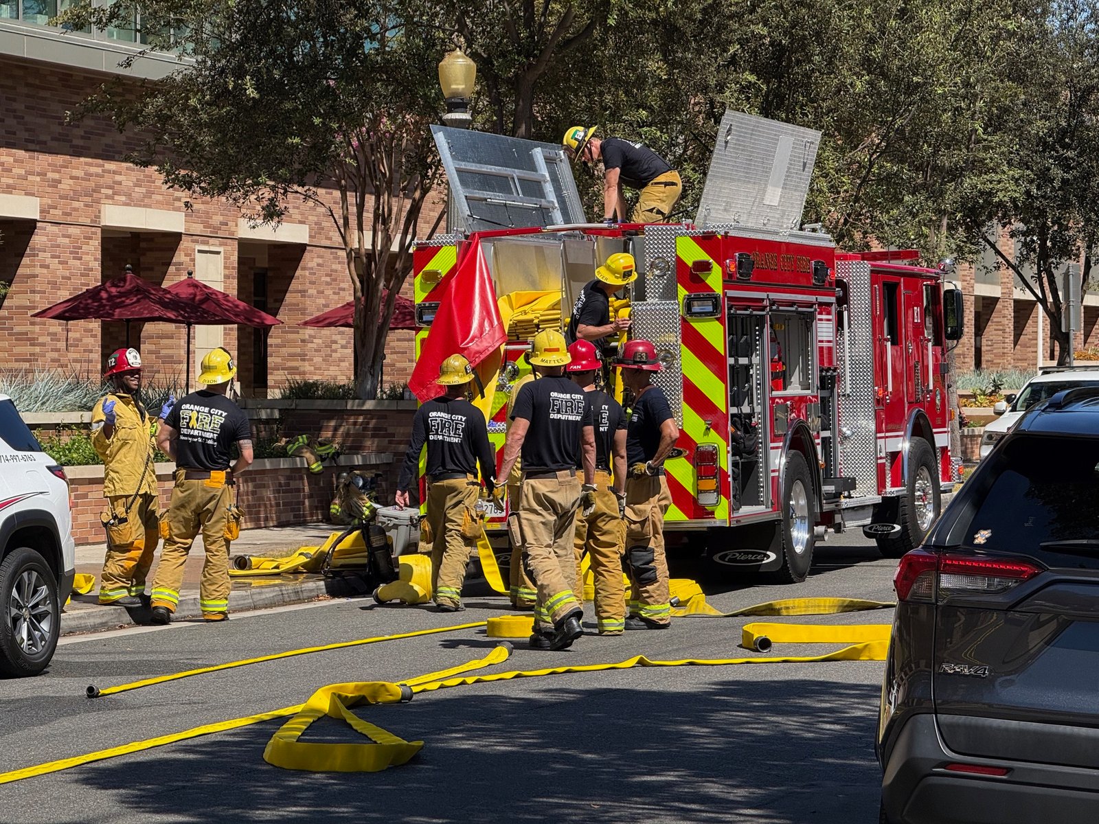 Firefighters gathered beside the rear of a fire engine, with hoses laid across the street.