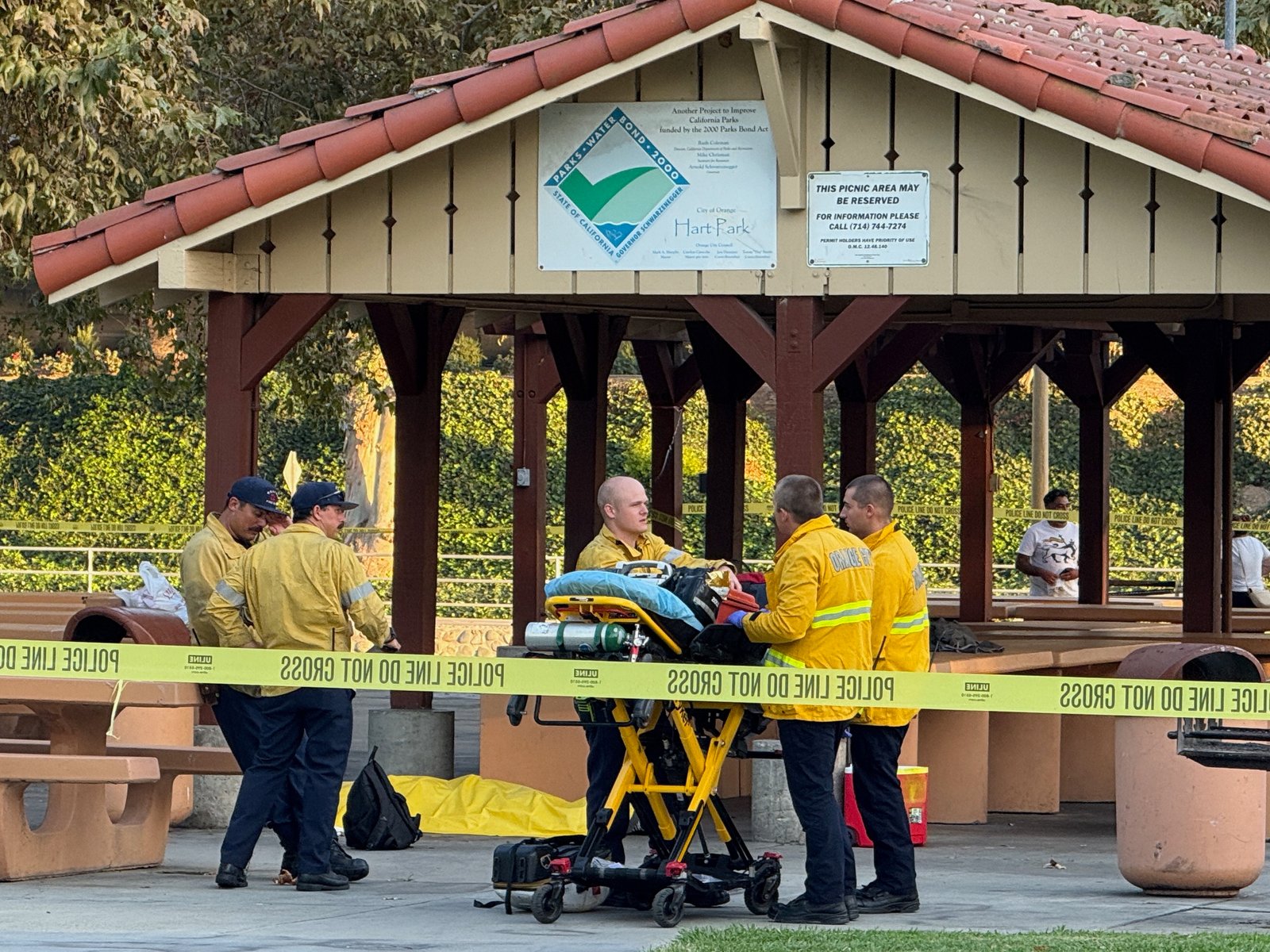 Firefighters and a stretcher behind police tape at Hart Park's covered picnic area.