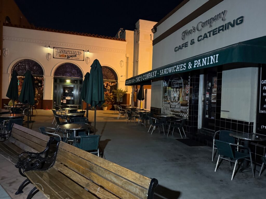 Outdoor seating beside Two's Company Cafe & Catering, with the neighboring storefront visible across the walkway.